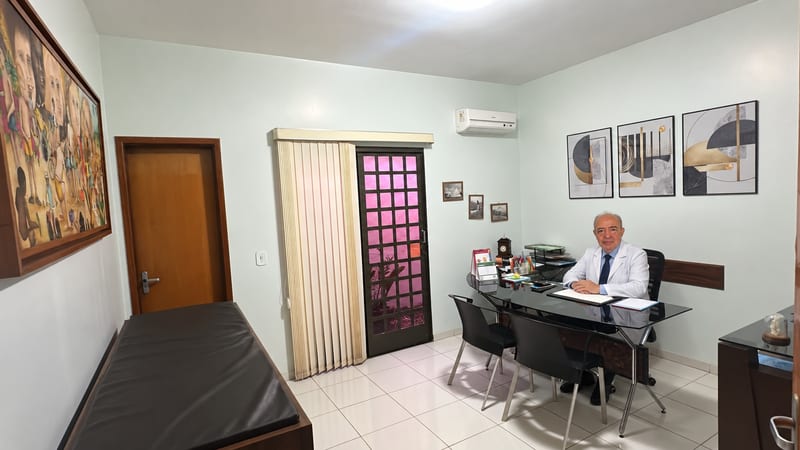 Sala de consulta do Imune Consultórios, com mesa de atendimento e maca, e o Dr. Paulo Prado à mesa, em Rio Verde